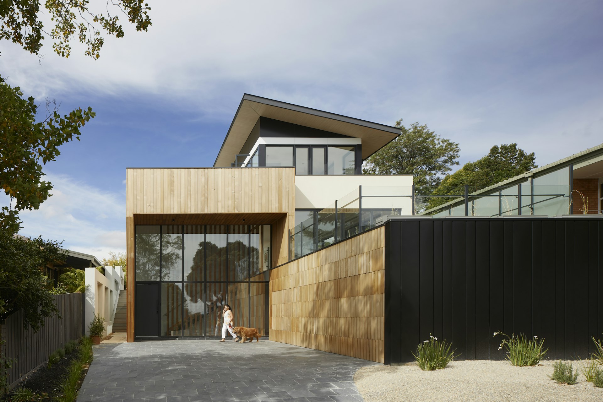 Contemporary home with wood and glass exterior, floor-to-ceiling windows, and a stone driveway under a clear sky